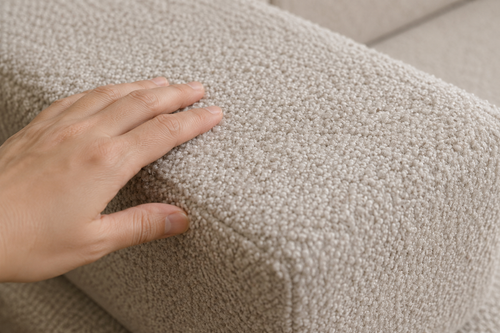 Close-up of hand touching beige bouclé floor cushion sofa texture for comfort and style.