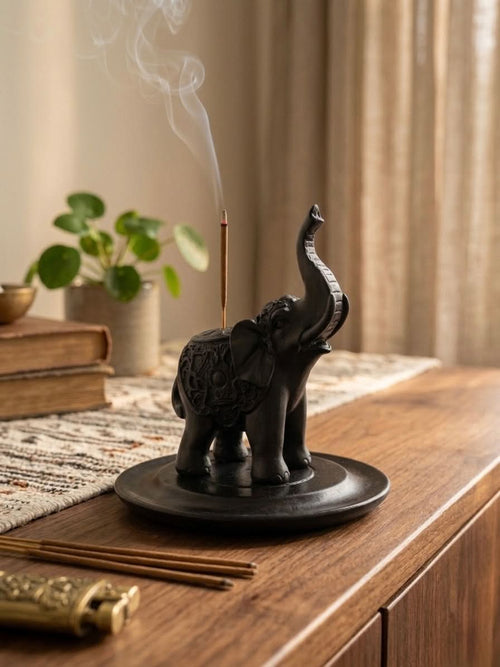 Black Elephant Incense Stick Holder with smoke rising, on a wooden table with decor