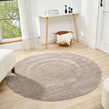 Beige round area rug displayed in a minimalist living room setting with natural light.