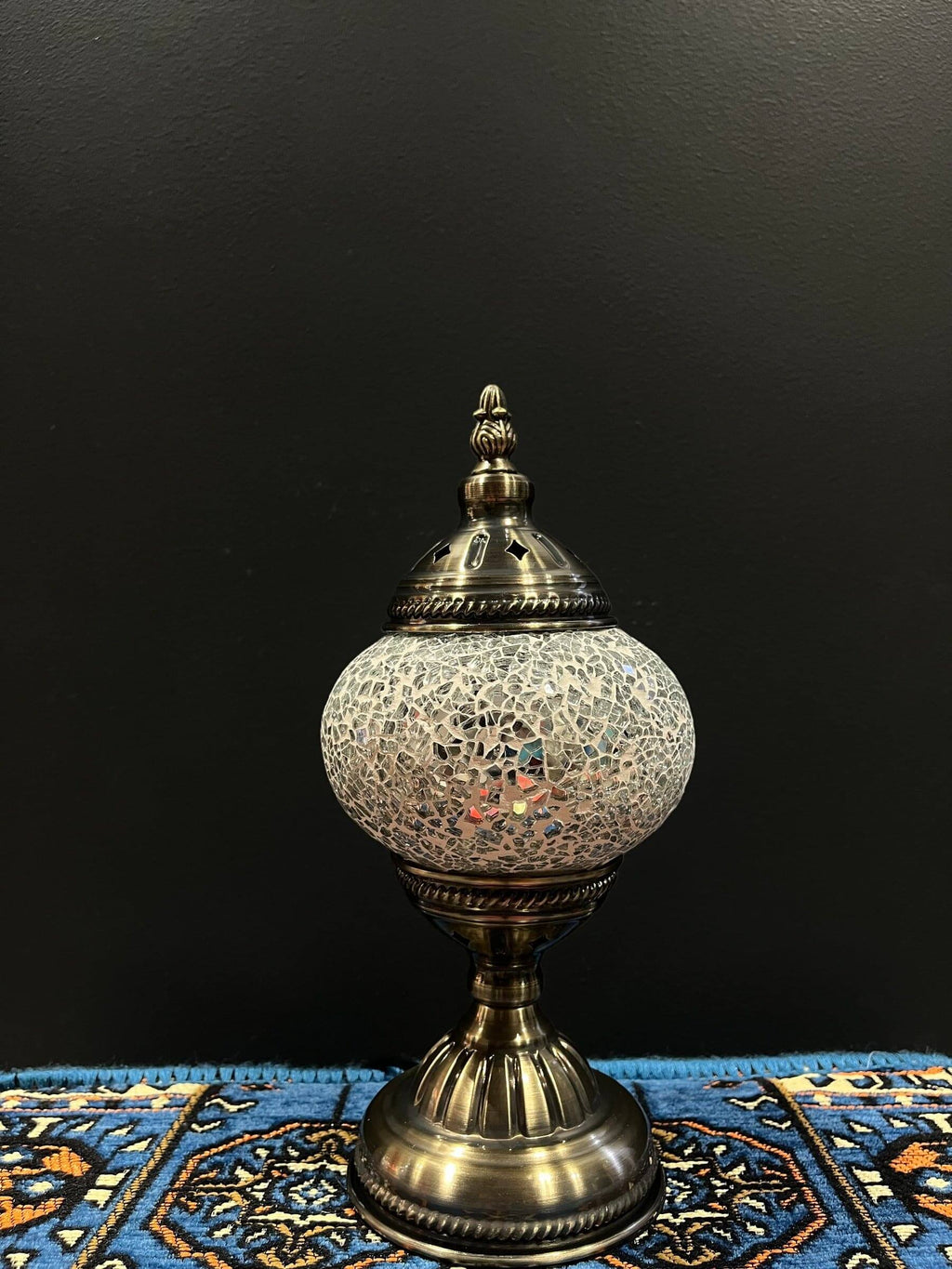 Mosaic Table Lamp with white crackle glass shade and decorative base on colorful rug.