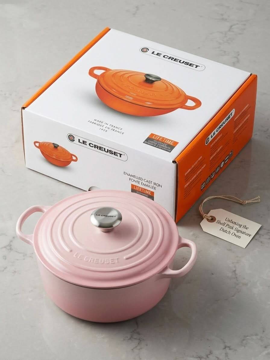 Le Creuset shell pink cast iron pot displayed with packaging on a marble countertop.