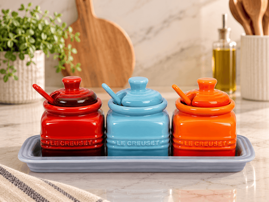 Le Creuset Ceramic Condiment Pot Set with red, blue, and orange pots on a tray for stylish kitchen storage.