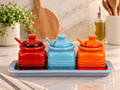 Le Creuset Ceramic Condiment Pot Set with red, blue, and orange pots on a tray for stylish kitchen storage.