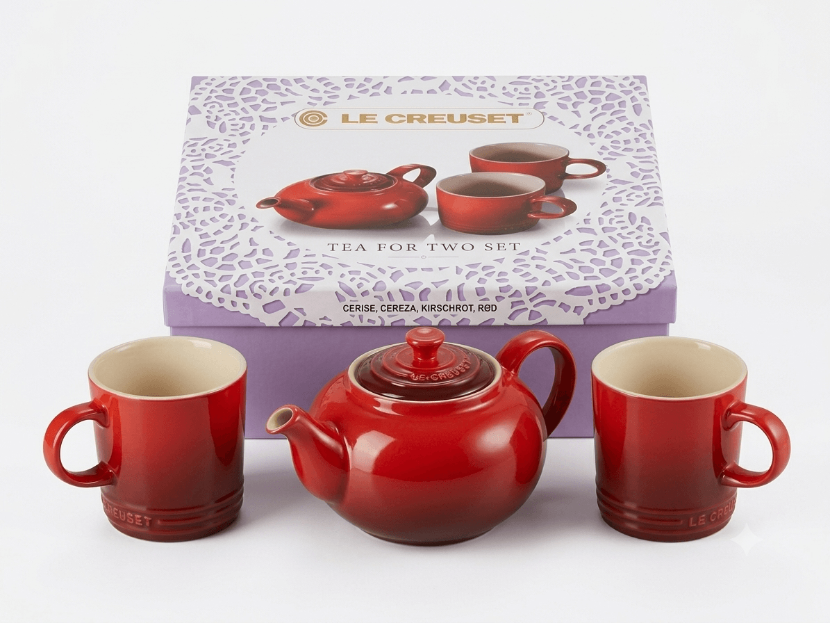 Le Creuset teapot with mugs set displayed with packaging, featuring a cerise red teapot and matching mugs.