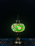 Mosaic Table Lamp with green and white glass mosaic design, illuminating warm light against a dark backdrop.