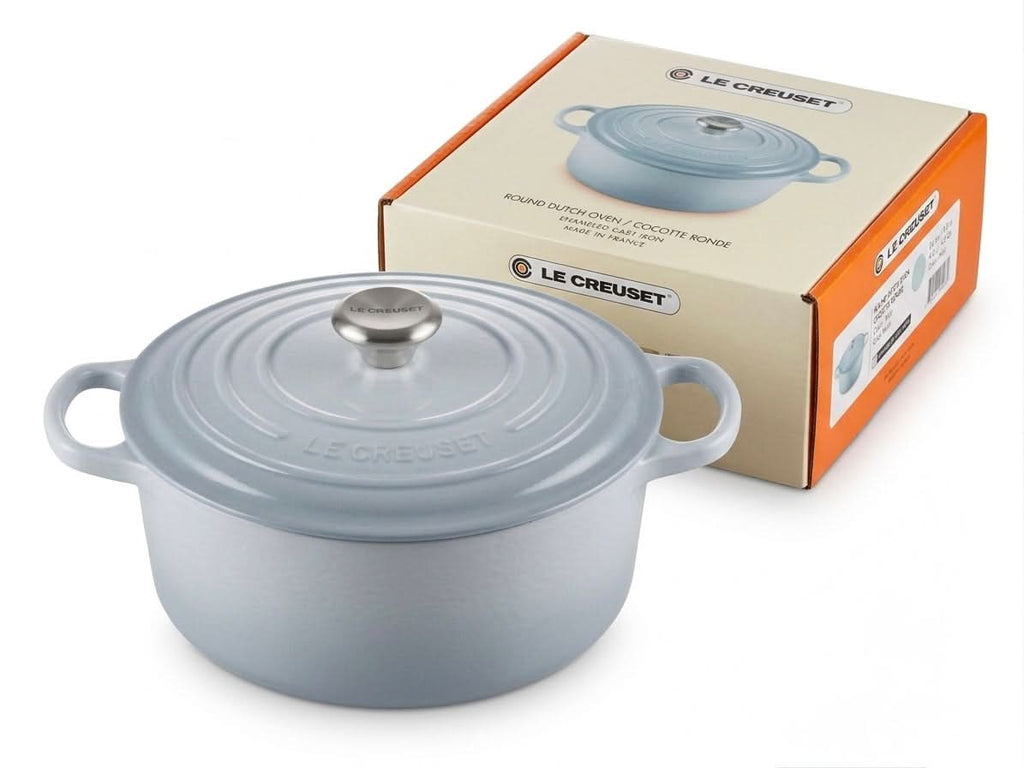 Le Creuset round Dutch oven 24cm in light blue color with lid next to its box, showcasing its premium design.