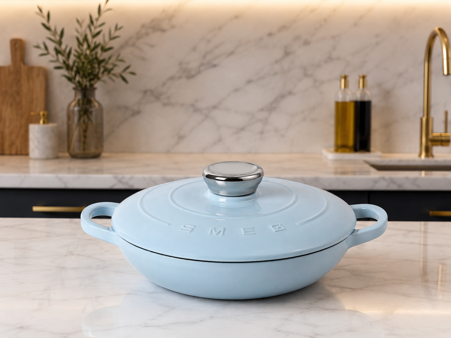 SMEG Cast Iron Braiser 26cm in light blue, shown on a marble kitchen countertop, ideal for various cooking methods.