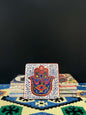 Stone Coaster Hamsa Hand White-Red-a captivating blend of ancient charm and artistic elegance. Crafted from genuine vintage stone, this coaster features the intricate Hamsa hand symbol, adding a touch of timeless mystique to your space. Sealed for durabil
