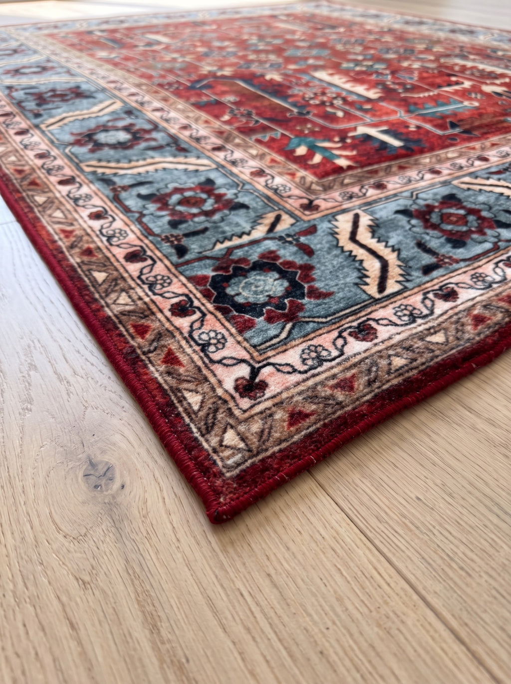 Anatolian Heritage rug corner showing the blue-grey patterned border and red bound edge