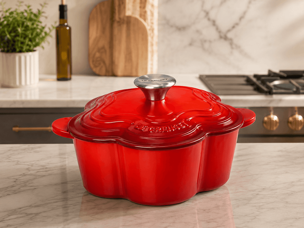 Le Creuset Flower Cocotte 20cm red on marble countertop with olive oil and greenery in background