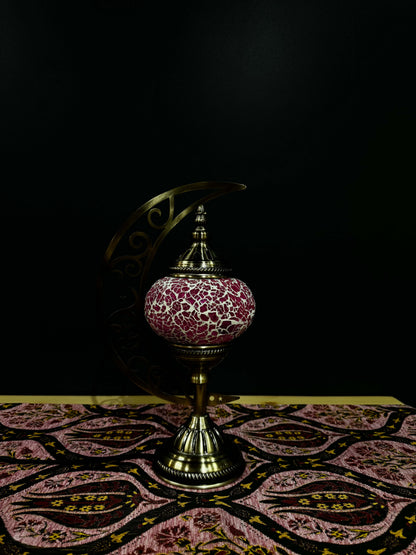 Rosy Glow Turkish mosaic table lamp with crescent moon design on patterned fabric background, radiating warm light.