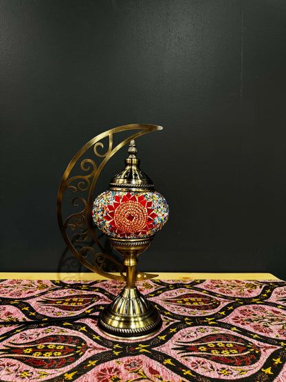 Sunburst Bloom Turkish Mosaic Lamp on a patterned tablecloth, featuring a crescent moon design and vibrant red mosaic.