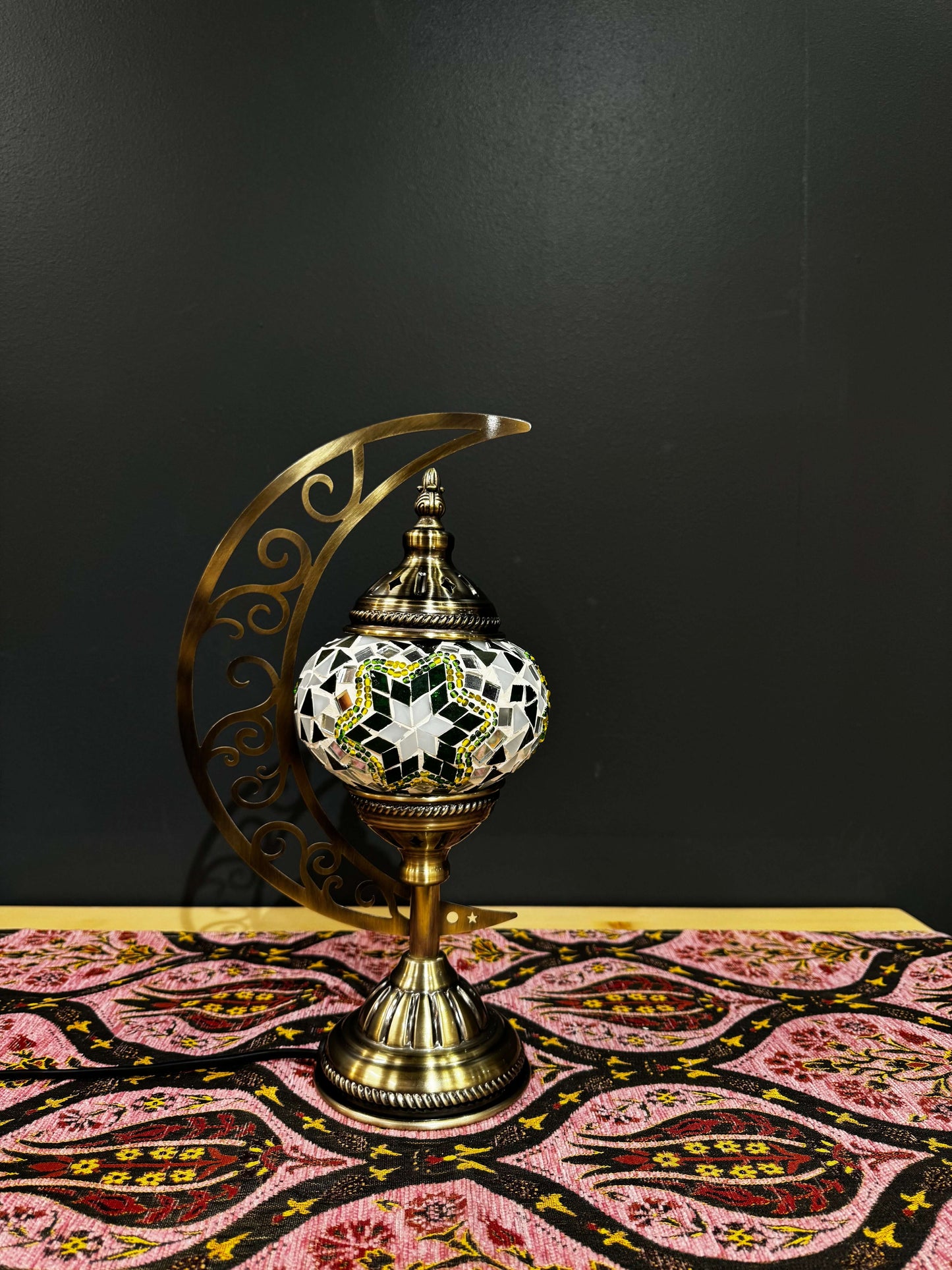 Emerald Star Turkish Mosaic Lamp with crescent moon design on a colorful tablecloth, showcasing radiant mosaic artistry.