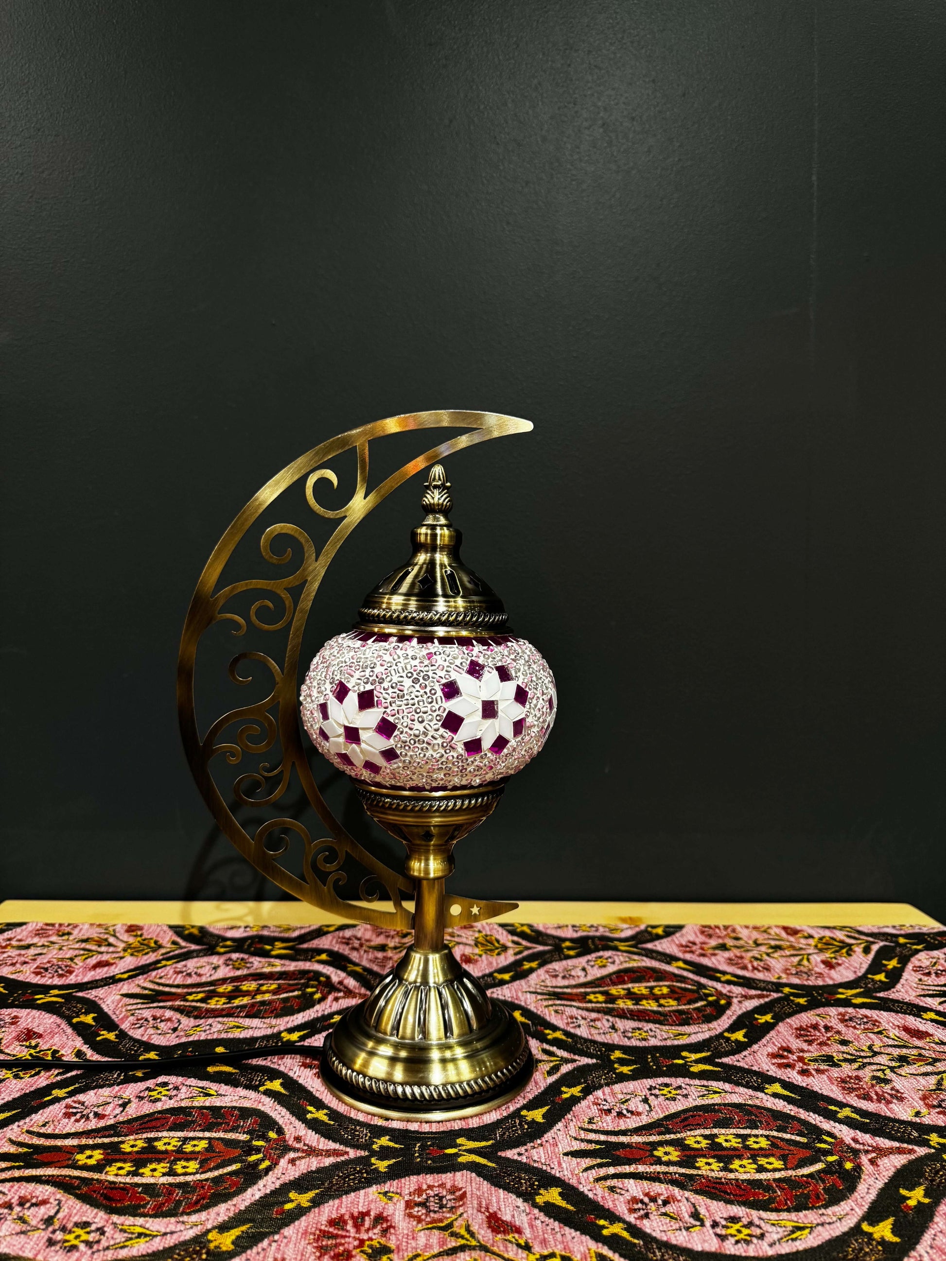 Pink Blossom Turkish Mosaic Lamp with crescent moon stand on patterned fabric, showcasing elegant floral design and warm glow.