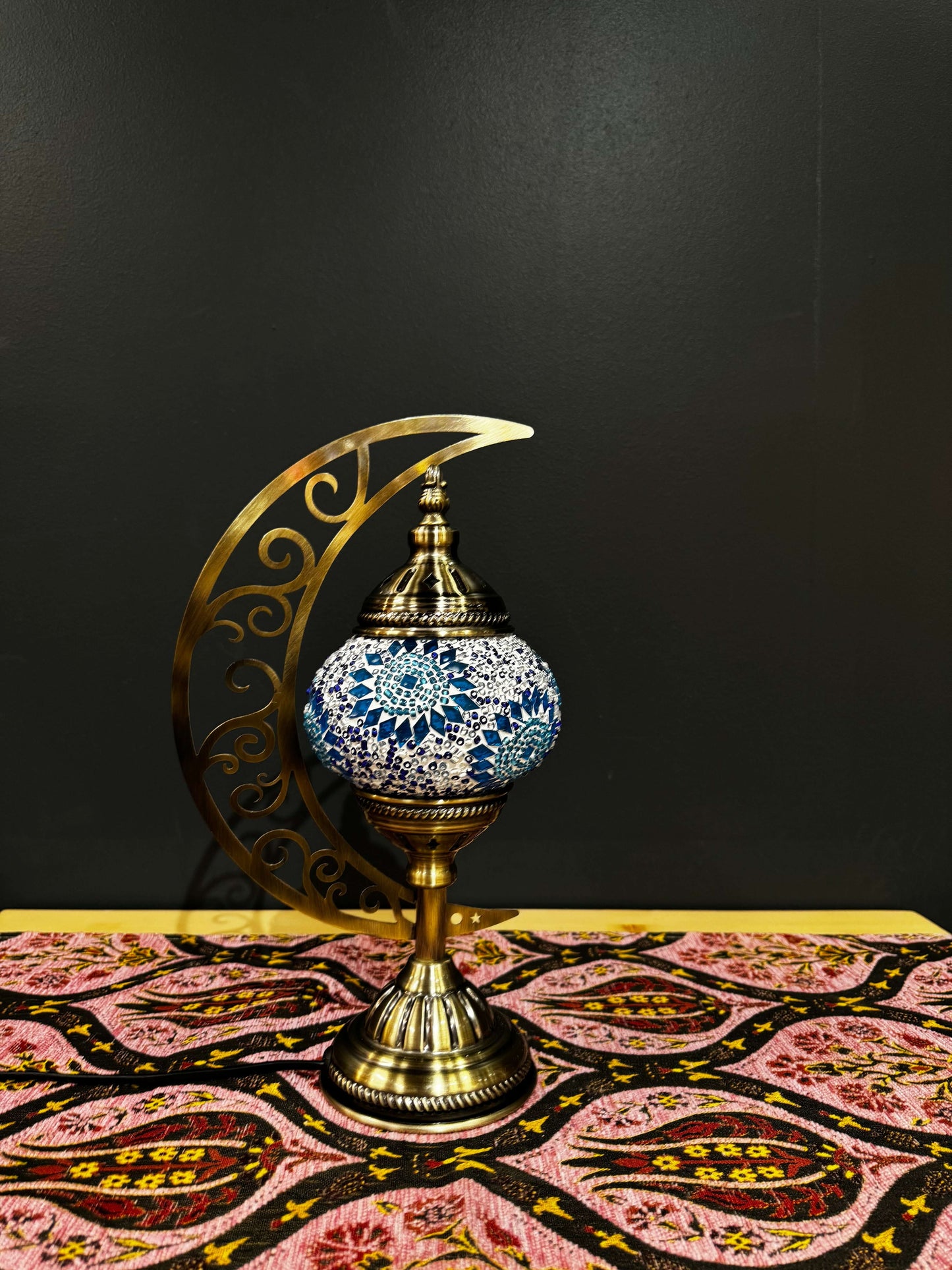 Turquoise Dream Turkish Mosaic Table Lamp with crescent moon stand on colorful patterned tablecloth.