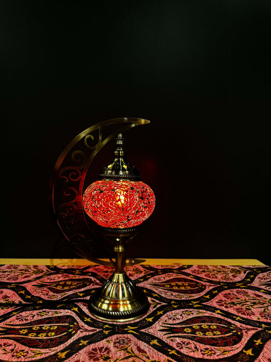 Crimson Glow Turkish Mosaic Lamp with crescent moon stand on decorated table, emitting warm red light. Perfect for elegant decor.