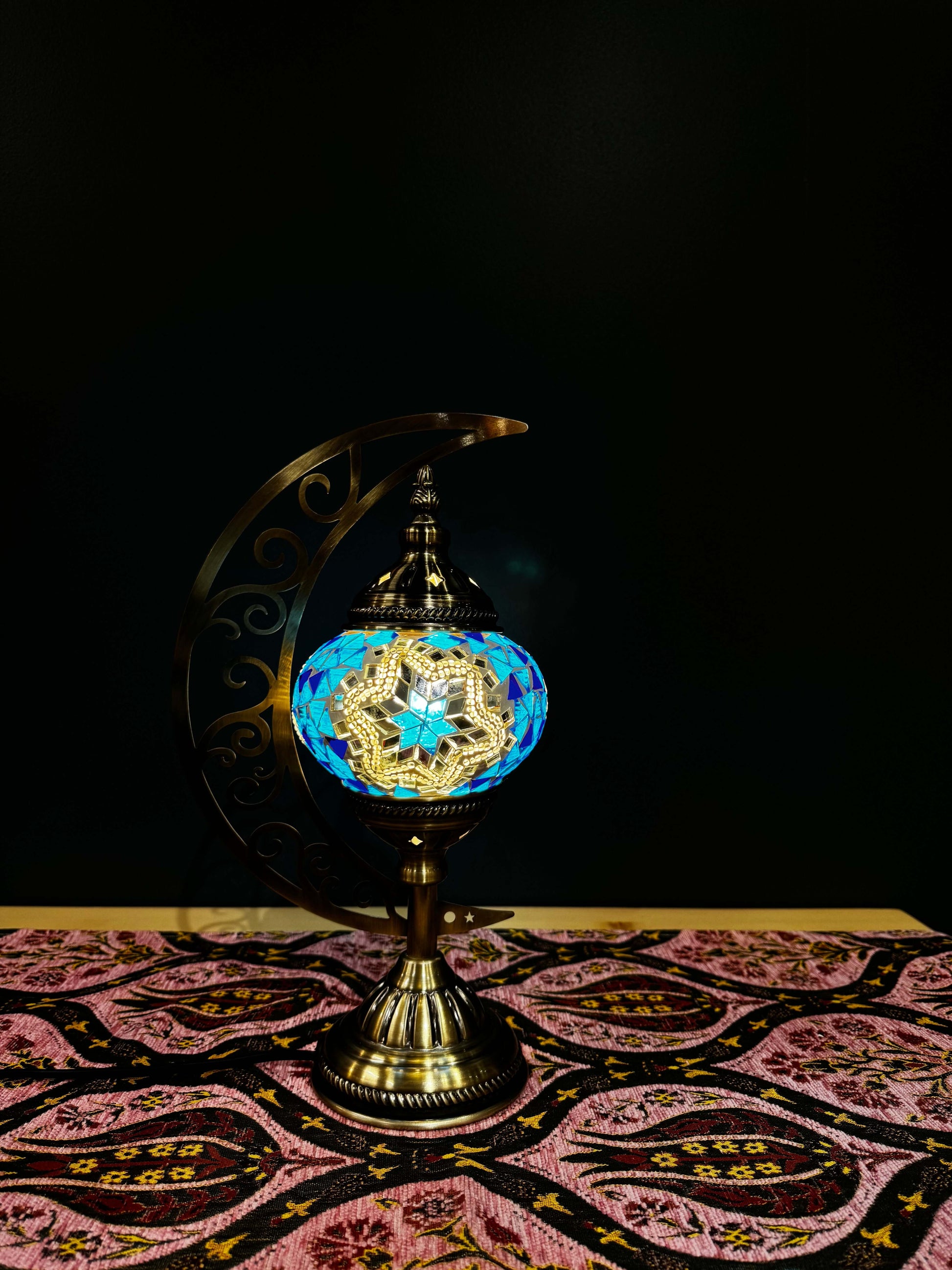 Azure Star Turkish Mosaic Lamp on a patterned table, featuring a crescent moon stand and vibrant blue mosaic design.