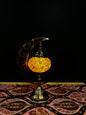 Amber Glow Turkish mosaic table lamp with crescent moon stand radiating warm light on a decorative tablecloth.