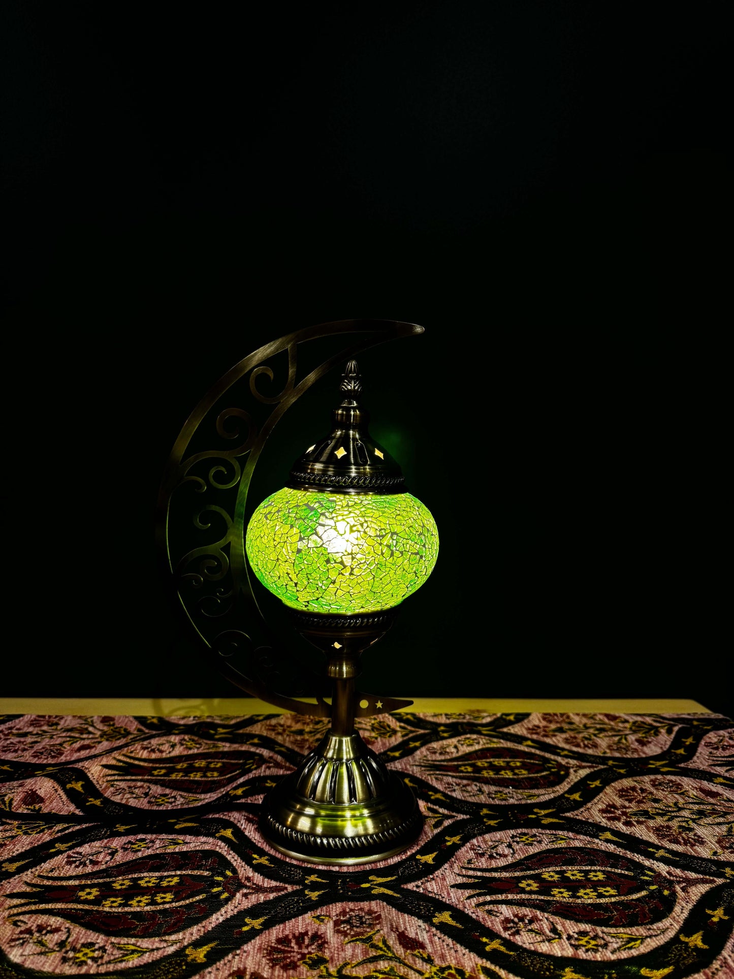 Lime Glow Turkish Mosaic Lamp on a patterned table, featuring a crescent moon design and vibrant crackled green mosaic.