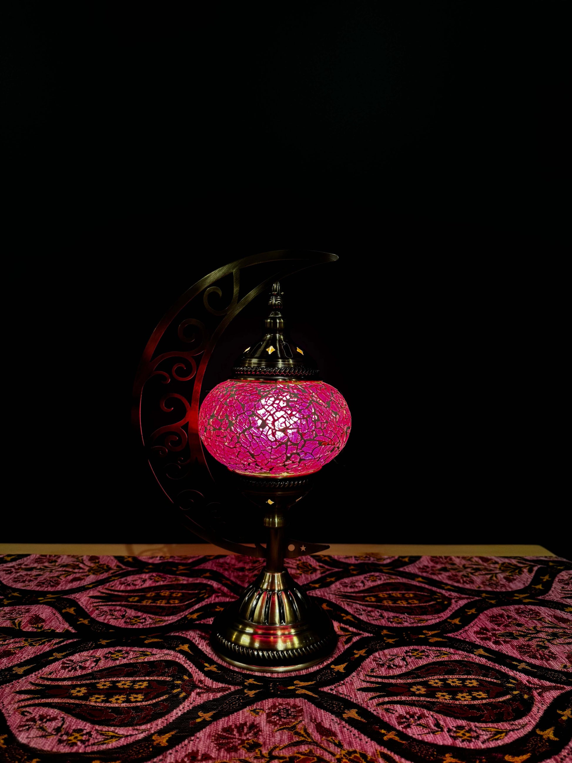 Rosy Glow Turkish Mosaic Lamp in pink on a decorative table, featuring a crescent moon metal stand, enhancing cozy ambiance.