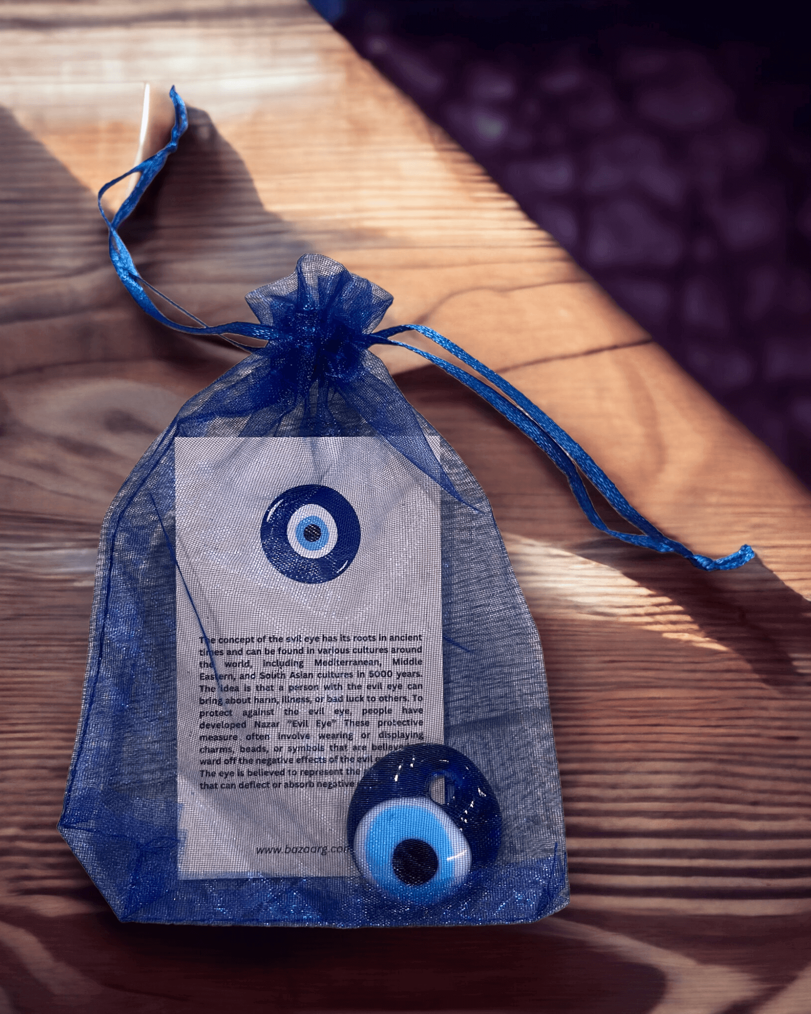 Evil Eye Bead (Nazar) in a blue bag with a protective charm description on a wooden surface.